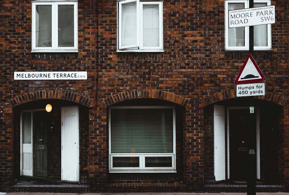Two traffic signs mounted on a stone and plaster wall in an alleyway; the larger, circular red sign with a white horizontal bar indicates no entry, while the smaller, circular blue sign with a white a