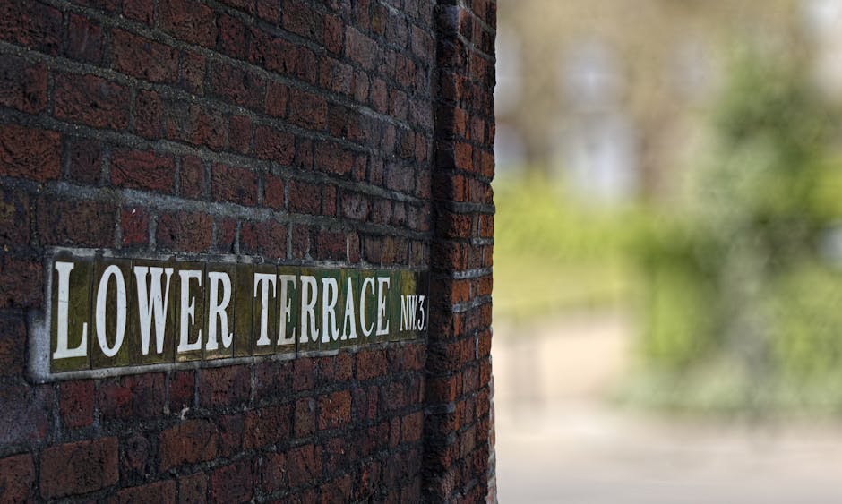 Close-up view of a brick exterior wall displaying a metal street sign for 'Lower Terrace NW3', with a portion of a doorway or entrance to a residential property visible on the left side. The sign has 